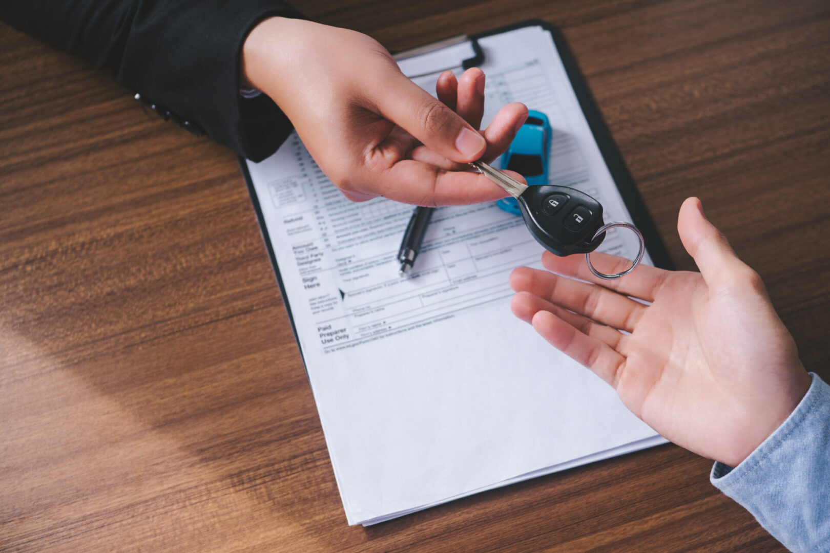 Concept car rental. Close up view Hand of agent giving car key to customer after signed rental contract form.